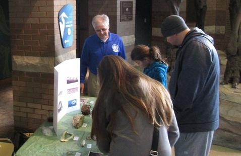 A museum guide showing geological specimens to a family at a display table.
