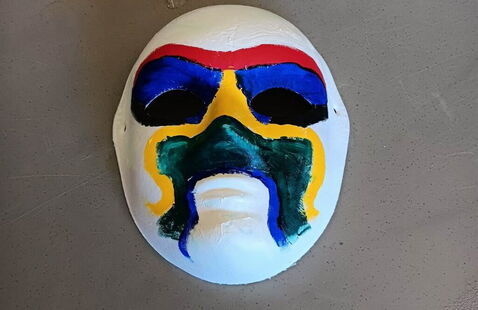 A white oval mask painted with red, blue, yellow, and green designs around the eye holes and mouth area.